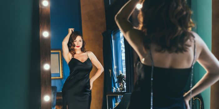 Woman in a black cocktail dress looking in a mirror