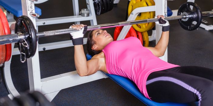 Woman in pink top doing barbell press ups in the gym